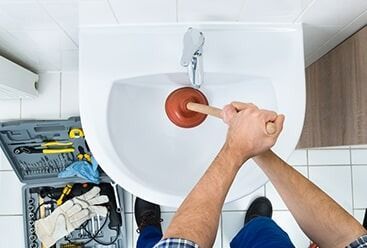 A Man is using a Plunger to fix a Sink — Plumbers & Gas Fitters in Coconut Grove, NT