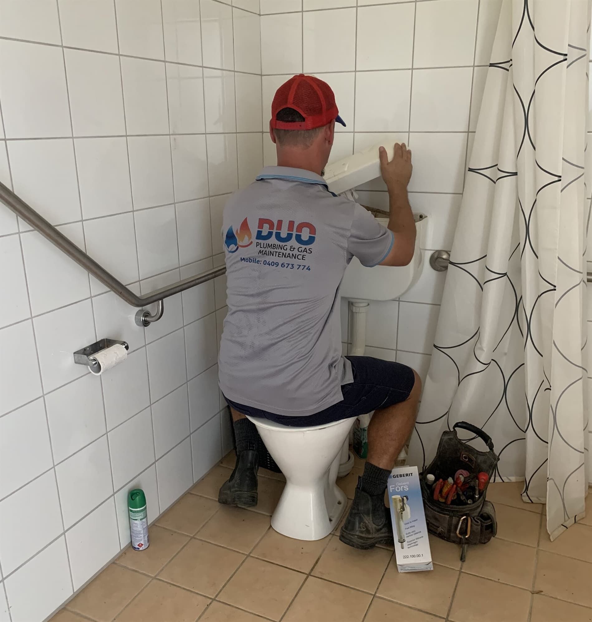 A Man is Sitting on a Toilet in a Bathroom — Plumbers & Gas Fitters in Coconut Grove, NT
