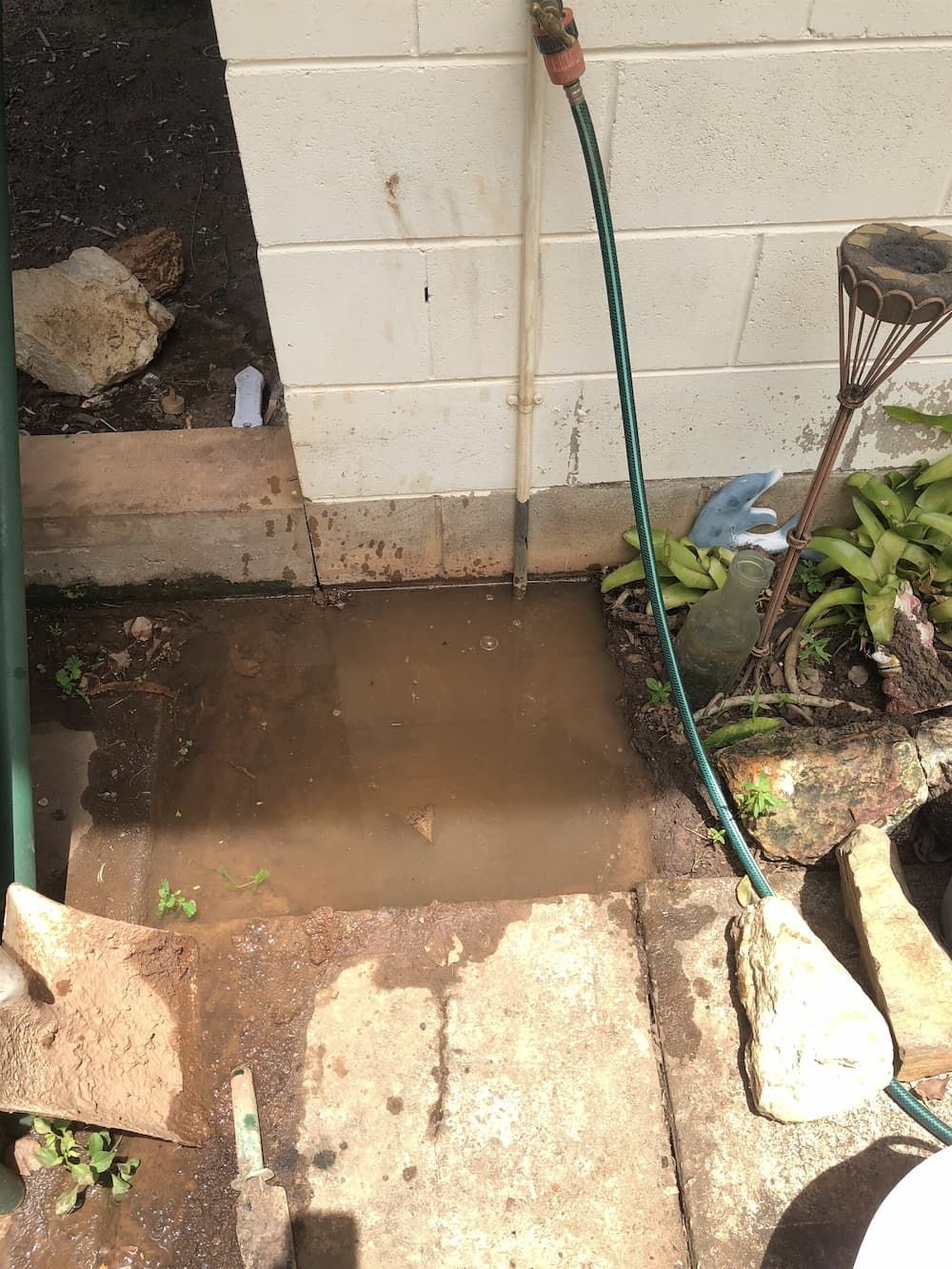 A Green Hose Is Connected to A Drain on The Side of A Building — Plumbers & Gas Fitters in Coconut Grove, NT