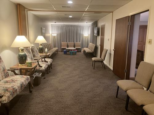 Waiting room with chairs, lamps, and a closed door. Dark carpet and neutral colors.