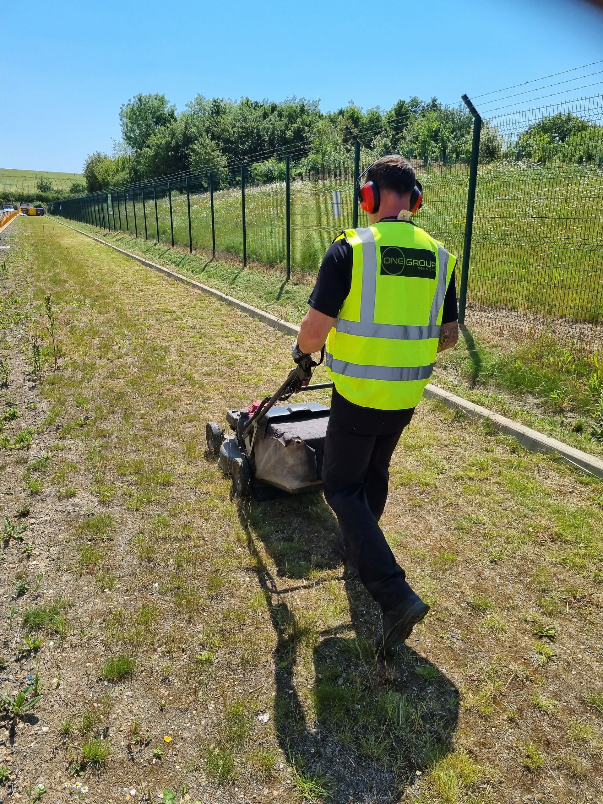 A man in a yellow vest is mowing the grass with a lawn mower.