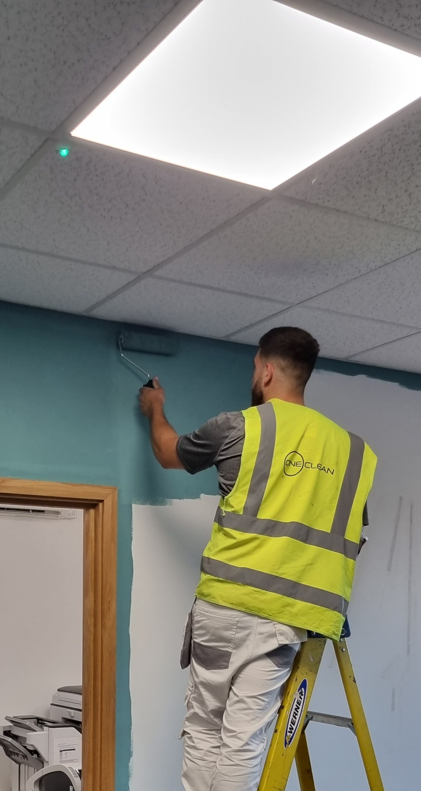 A man is standing on a ladder painting a wall.