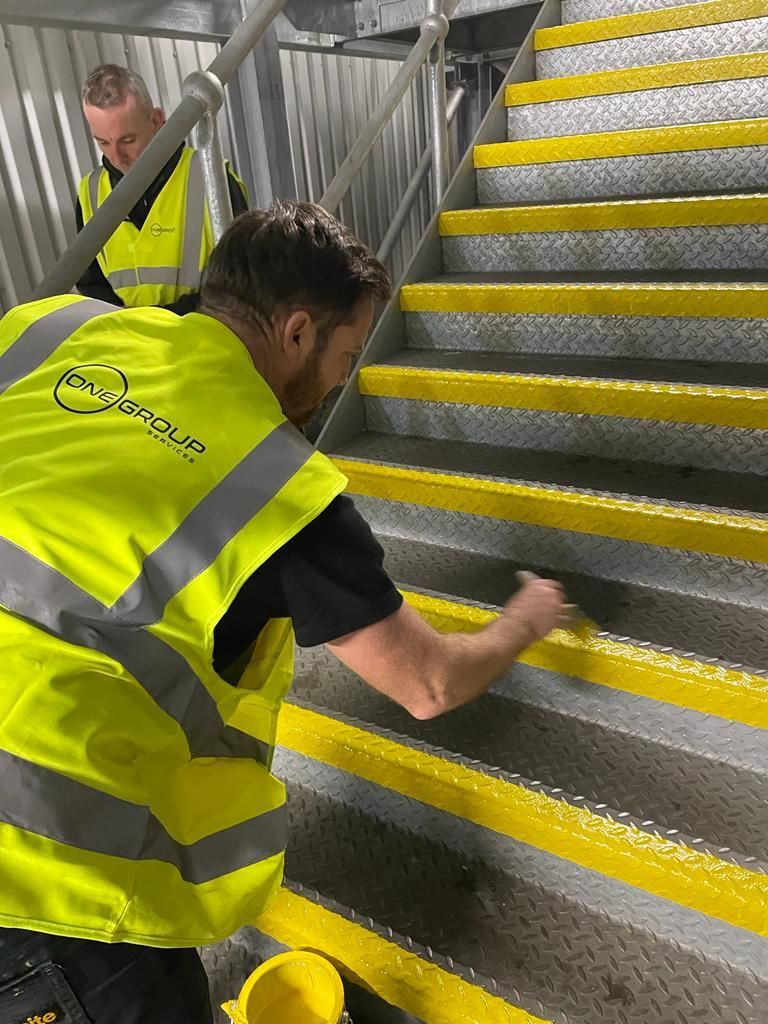 A man in a yellow vest is cleaning a set of stairs.