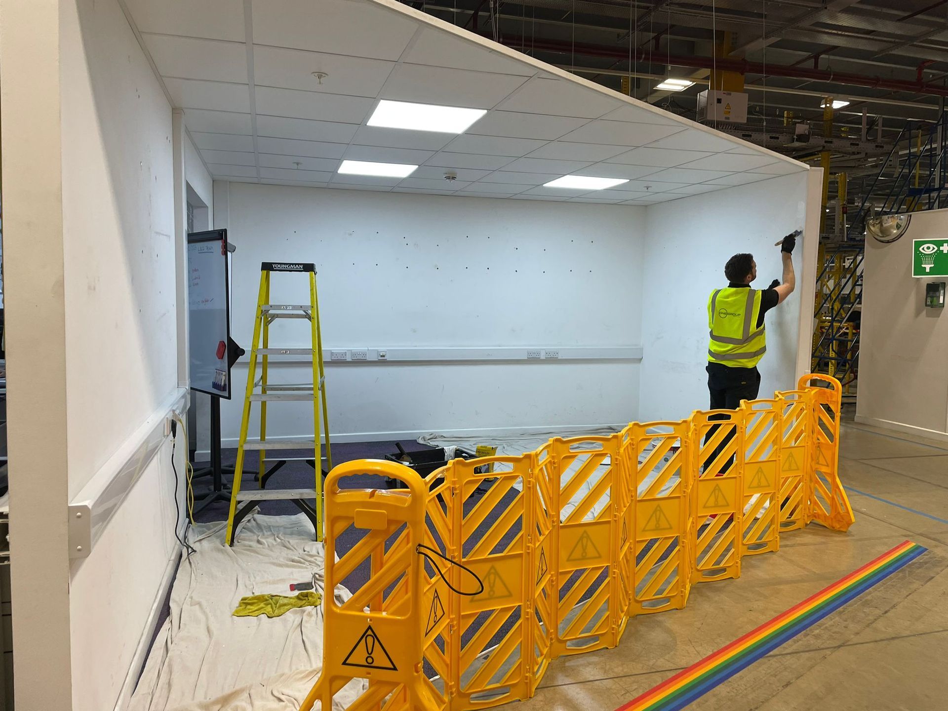 A man is painting a wall in a room with yellow barriers.