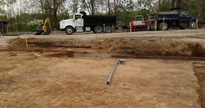 Construction site with a white dump truck, excavator, and dirt grading area with a pipe in the foreground