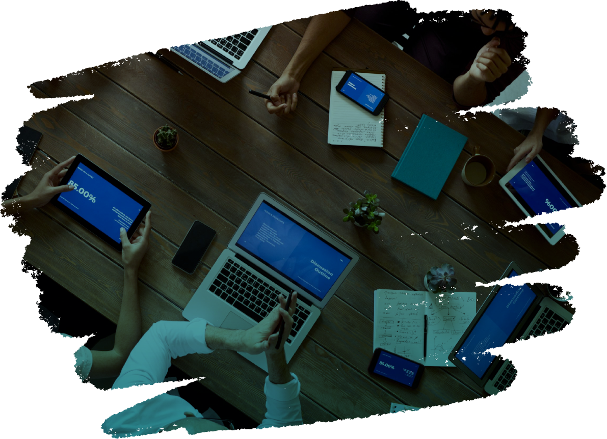 Um grupo de pessoas está sentado ao redor de uma mesa com laptops e telefones