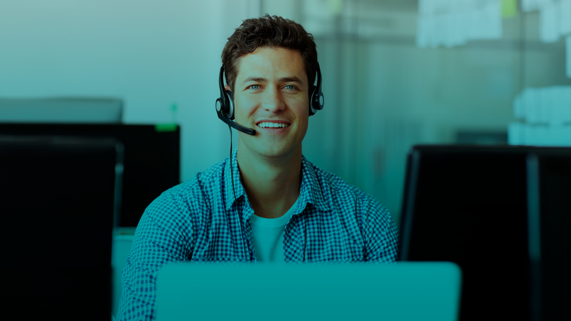 Um homem usando um fone de ouvido está sentado em frente a um laptop.