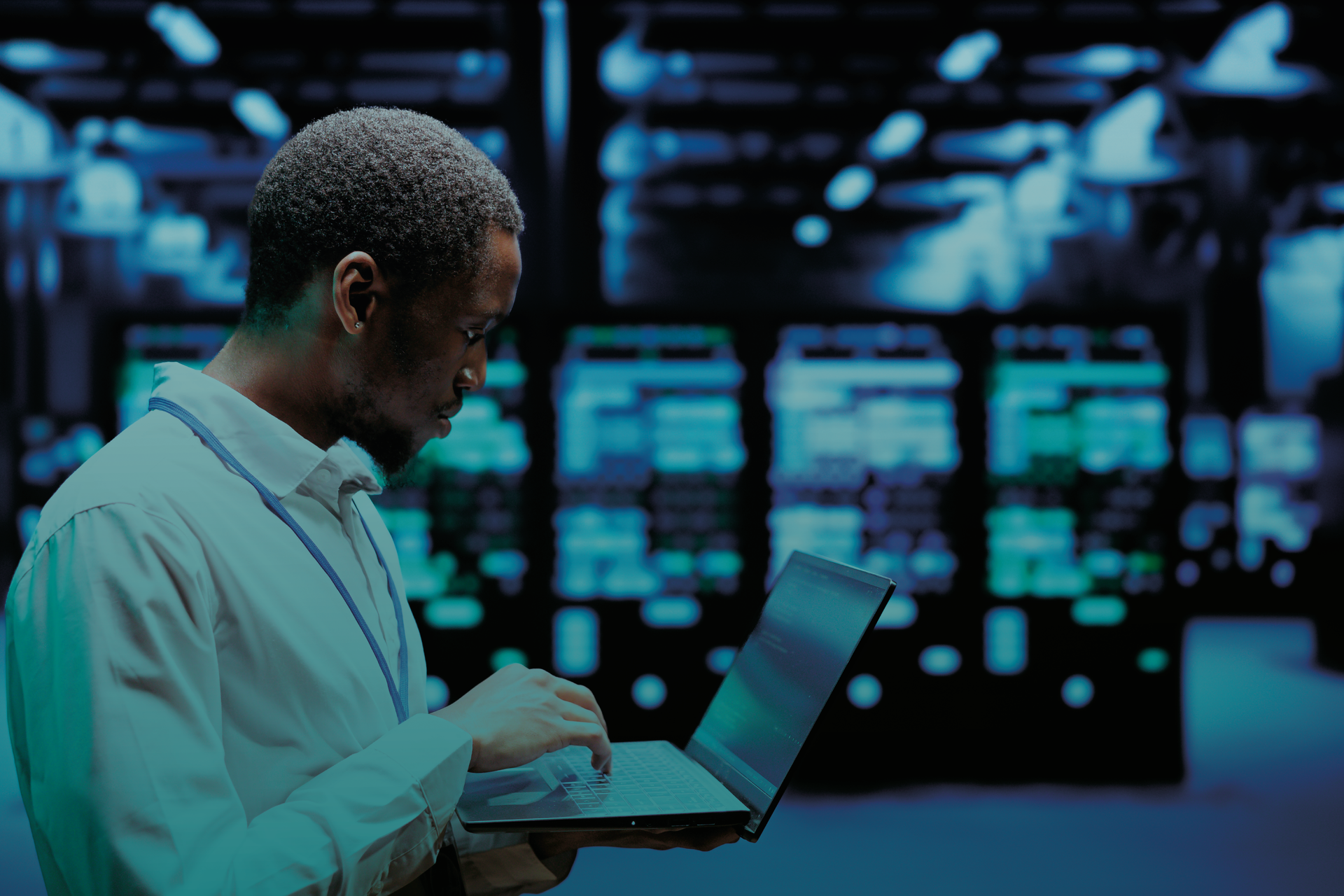 Um homem está usando um laptop em uma sala de servidores.