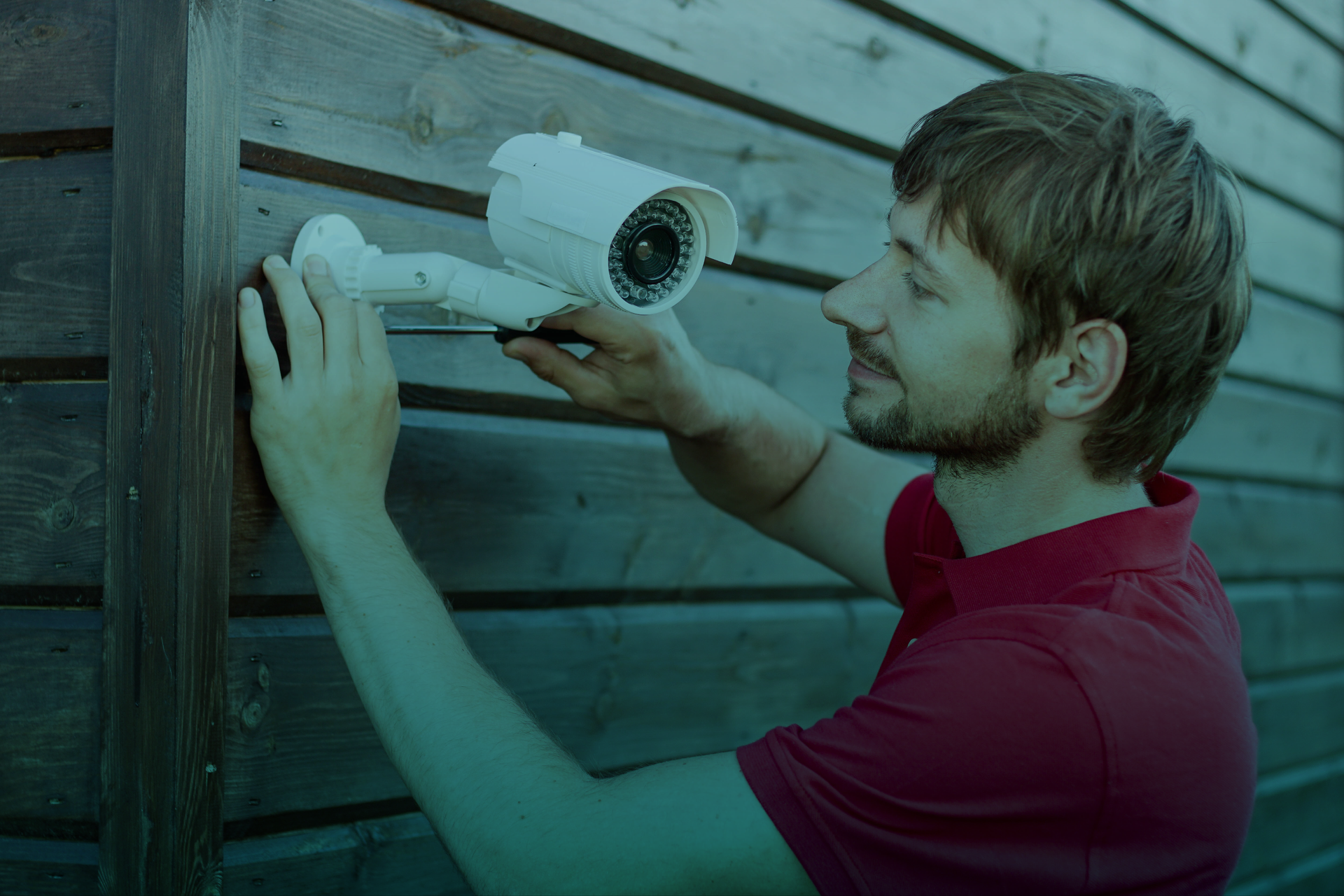 Um homem está instalando uma câmera de segurança em uma parede de madeira.