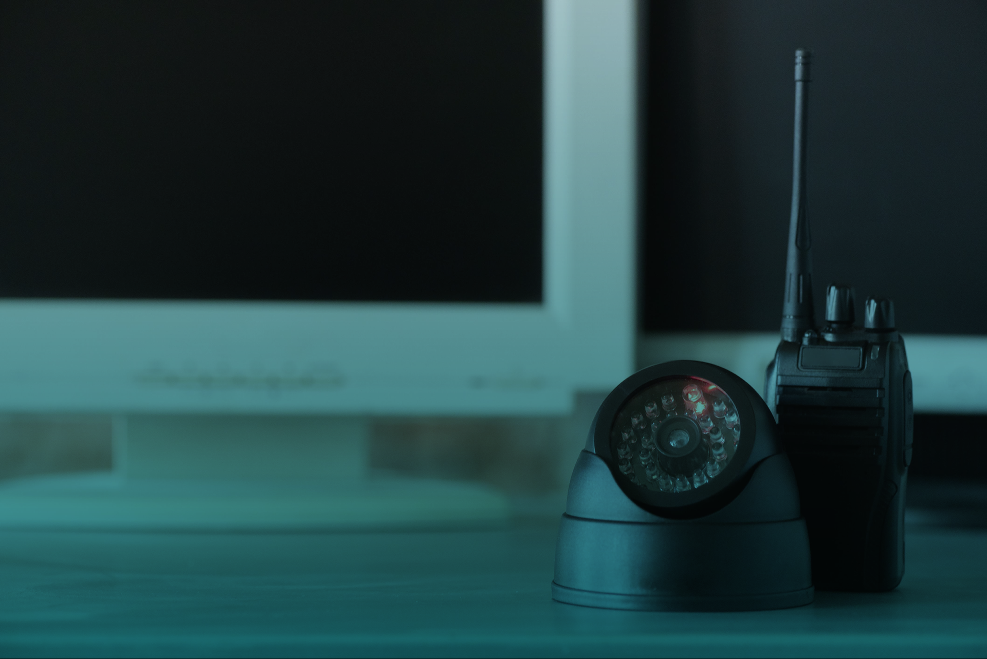 Uma câmera de segurança e um walkie talkie estão sobre uma mesa em frente a um monitor de computador.