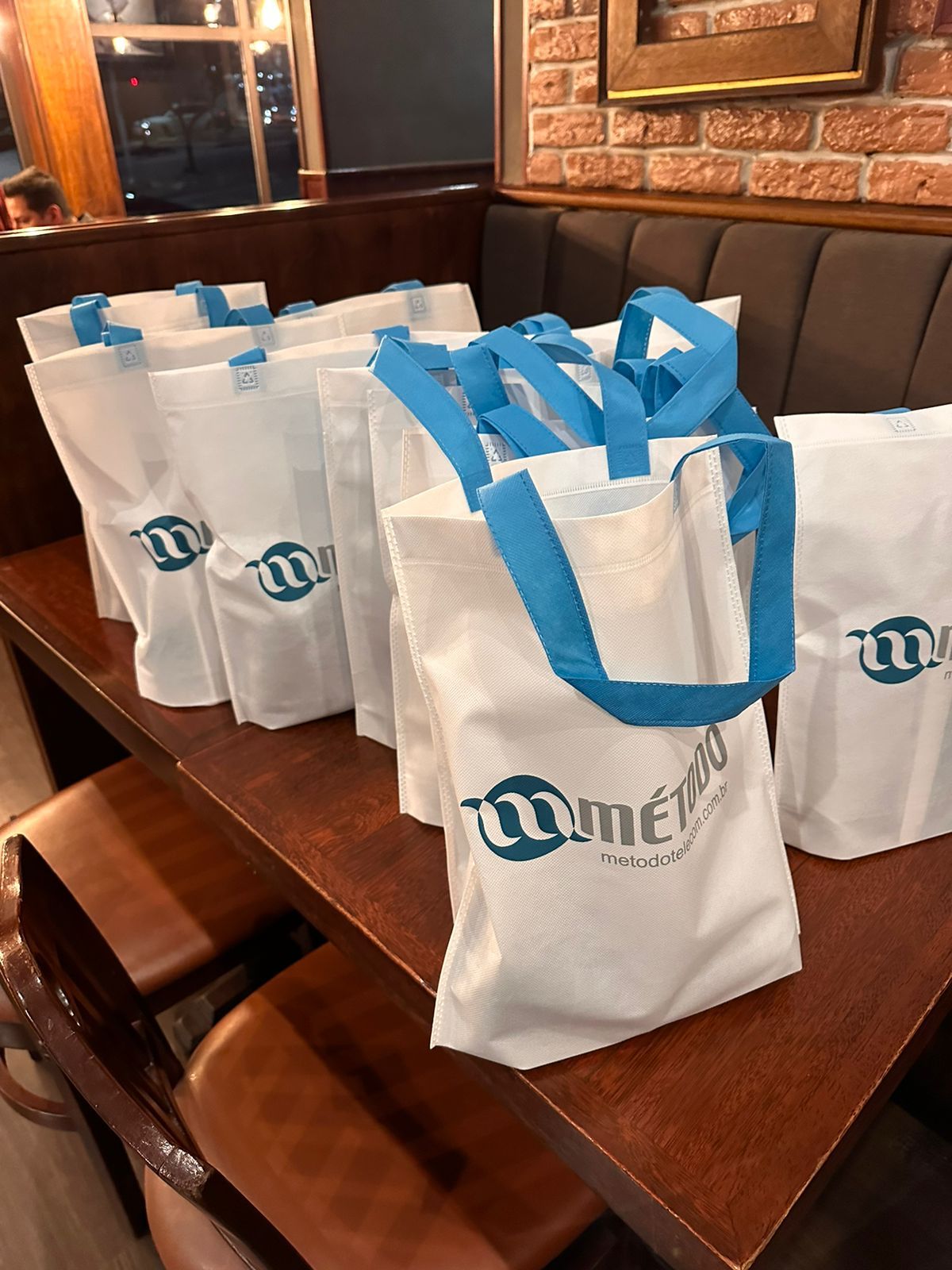 Uma fileira de sacolas brancas com alças azuis estão sobre uma mesa de madeira.