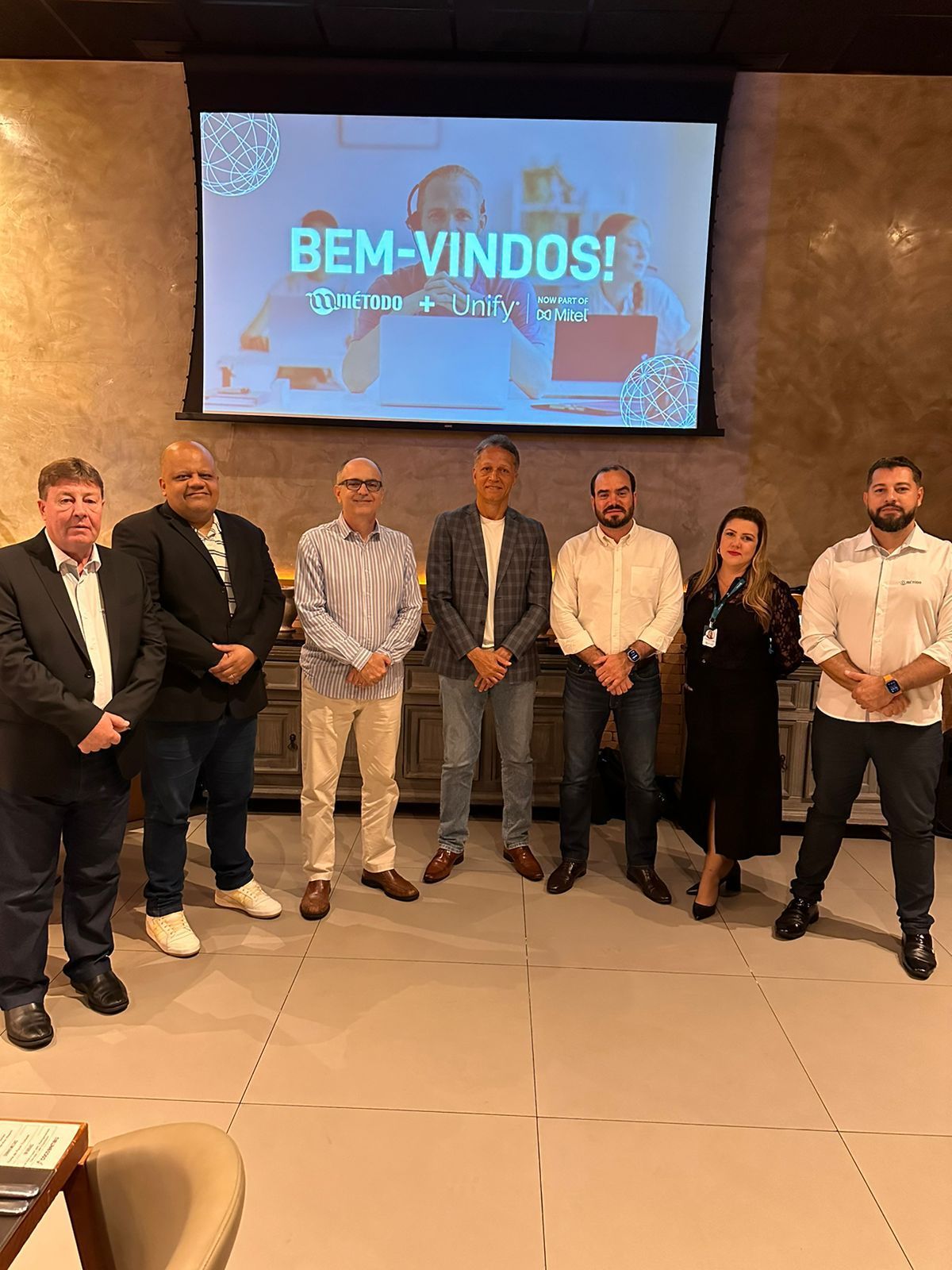Um grupo de pessoas está em pé em frente a uma tela grande.