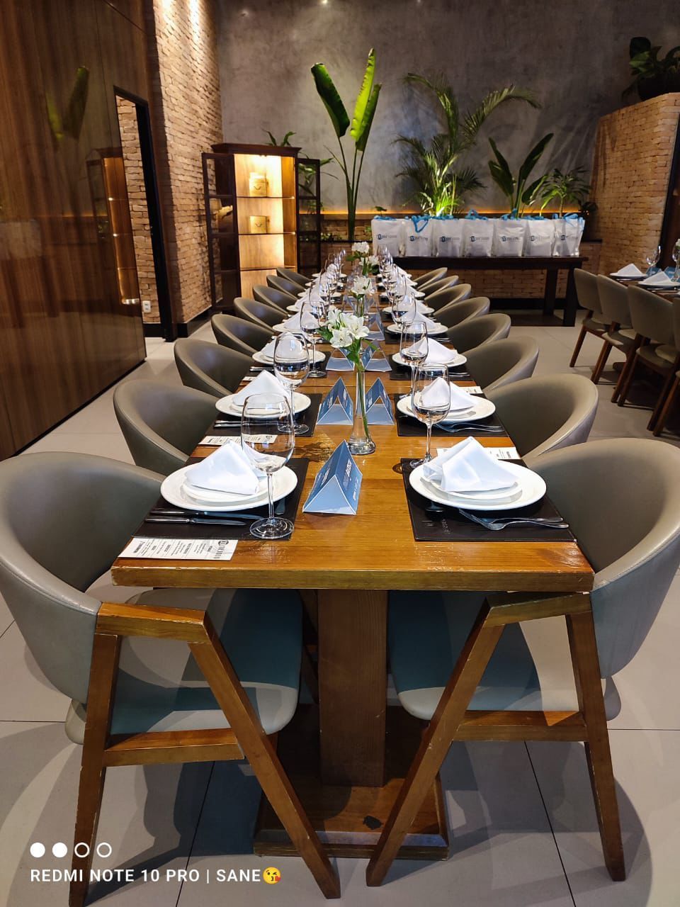 Uma mesa longa com pratos, utensílios e cadeiras em um restaurante.