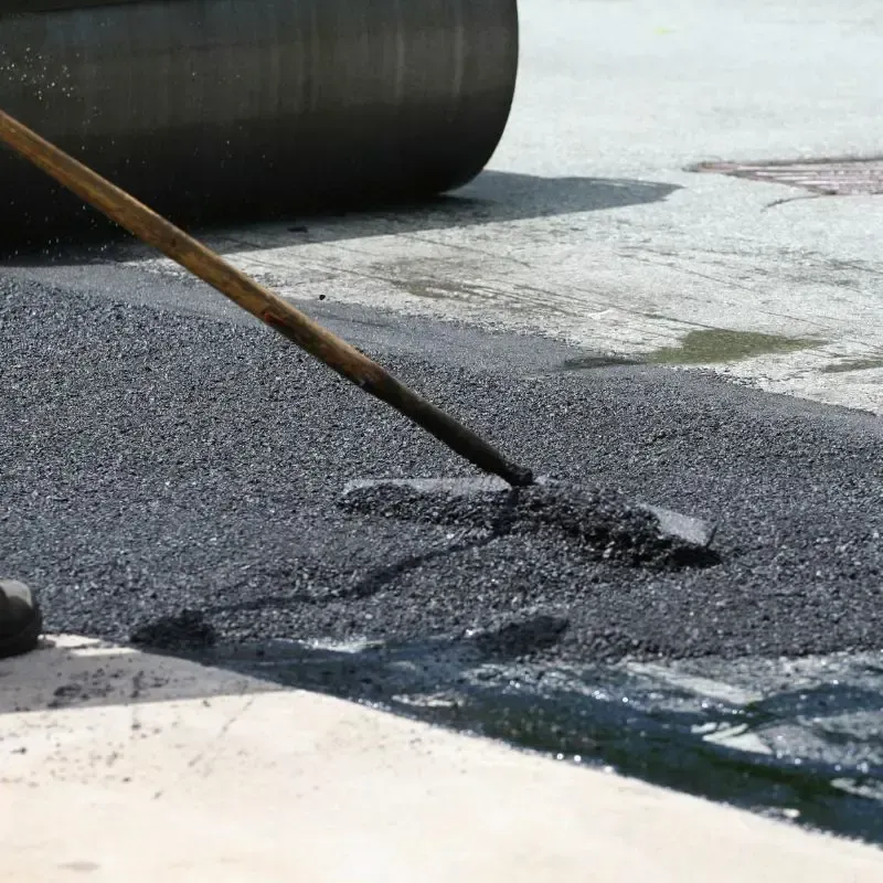 A person is using a broom to spread asphalt on the ground