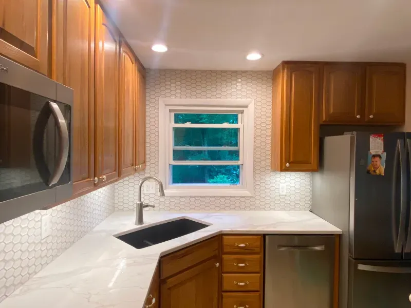 A kitchen with wooden cabinets , stainless steel appliances , a sink , and a window.