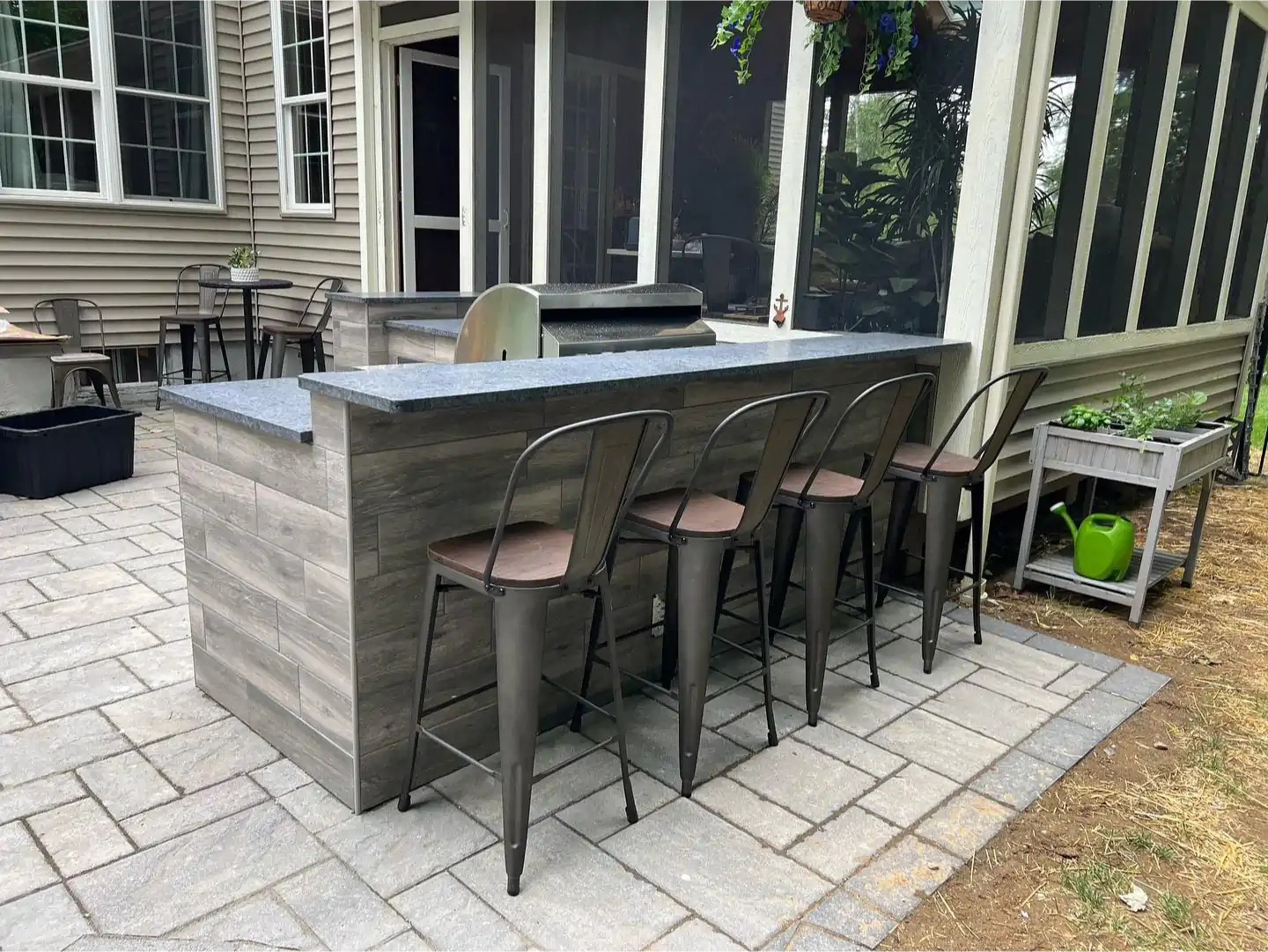A patio with a bar and chairs in front of a screened in porch.