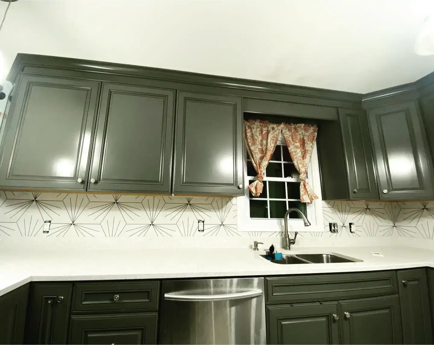 A kitchen with gray cabinets , a stainless steel dishwasher , a sink , and a window.