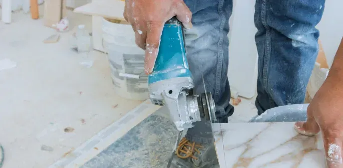 A man is cutting a tile with a grinder.