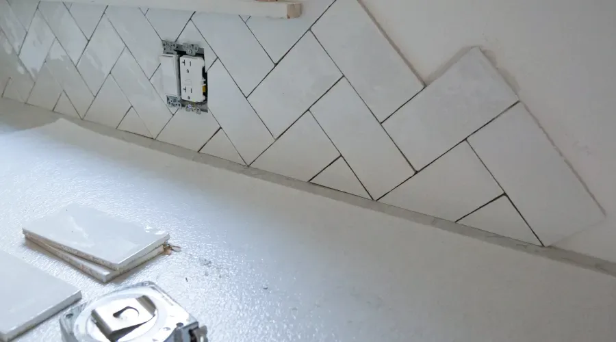 A herringbone tile wall is being installed in a kitchen.