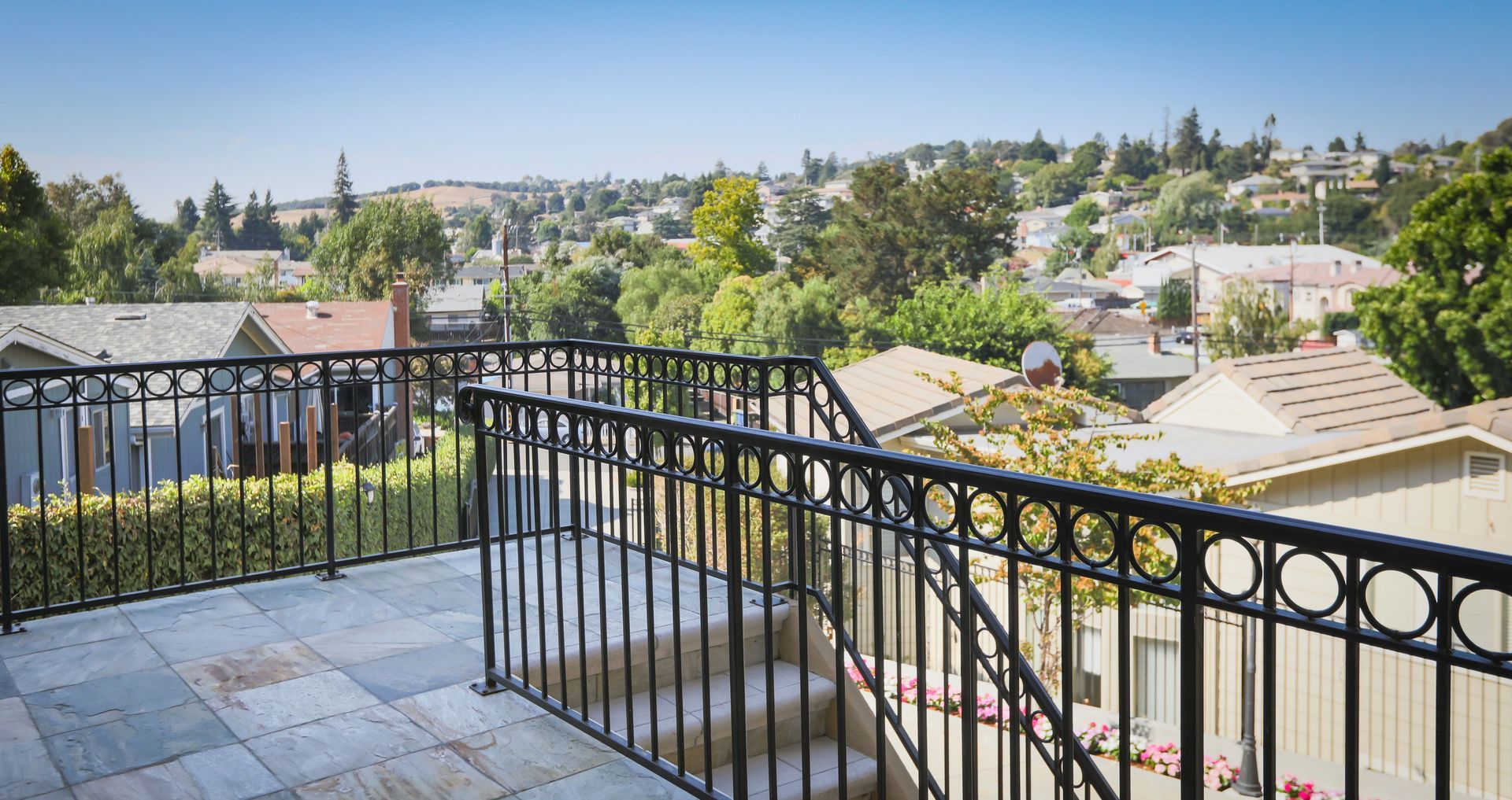 Balcony overlooking a sunny suburban neighborhood with black metal railings and tiled floor