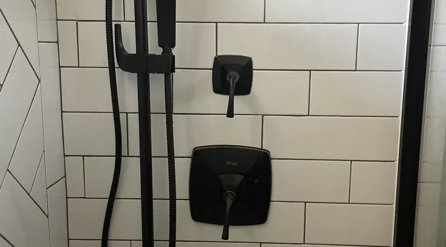 A black shower head is in a bathroom with white tiles.