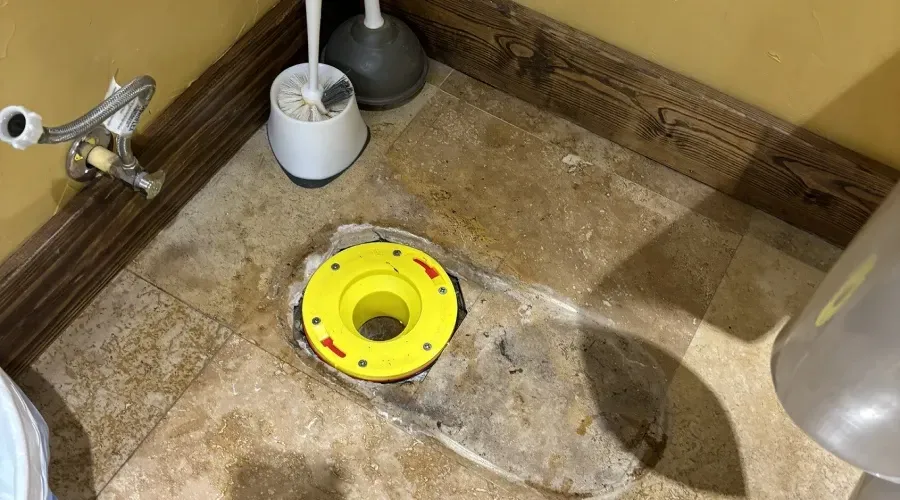 A toilet with a yellow flange on the floor next to a toilet brush.