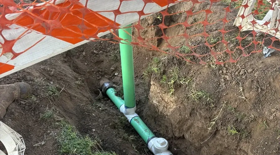 A green pipe is being installed in a hole in the ground.