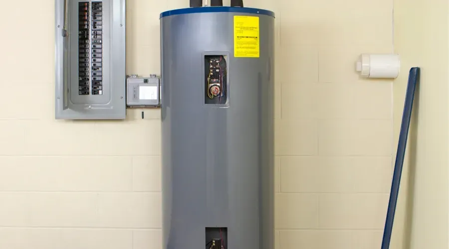 A water heater is sitting on a wall next to a mop.