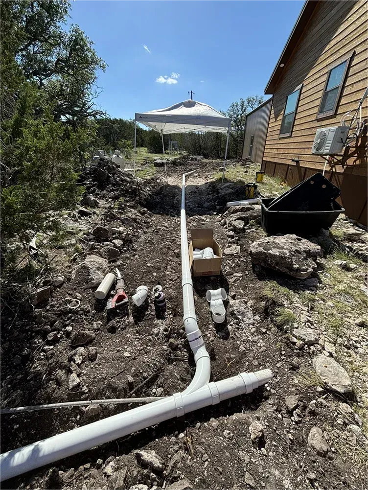 A pipe is being installed in the dirt in front of a house.