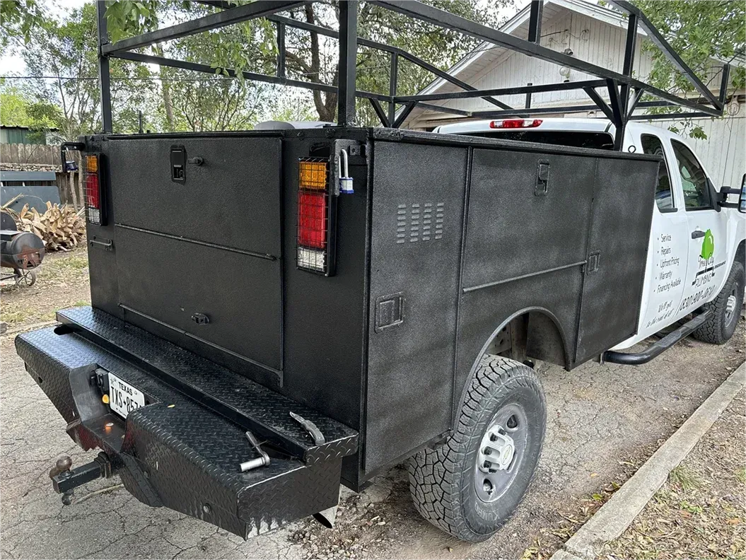 A white truck with a black utility bed is parked on the side of the road.