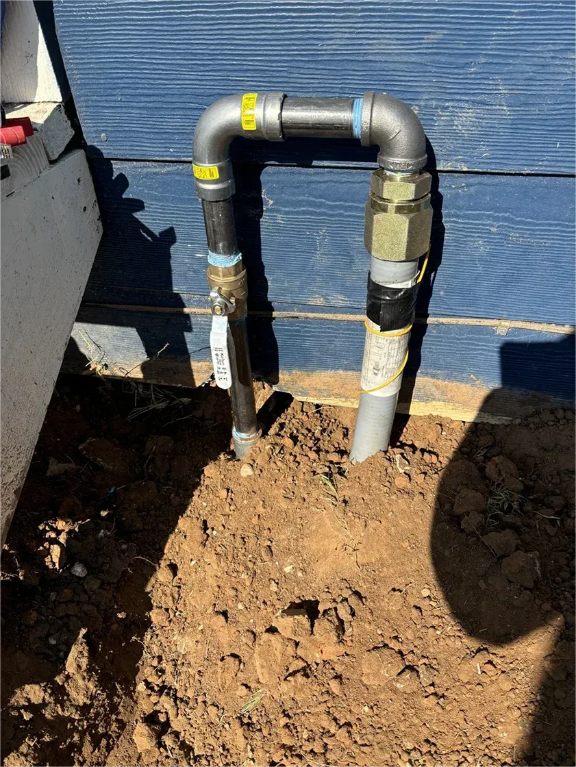 A pipe is sitting in the dirt next to a blue wall.