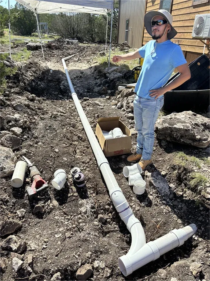 A man is standing next to a large pipe in the dirt.