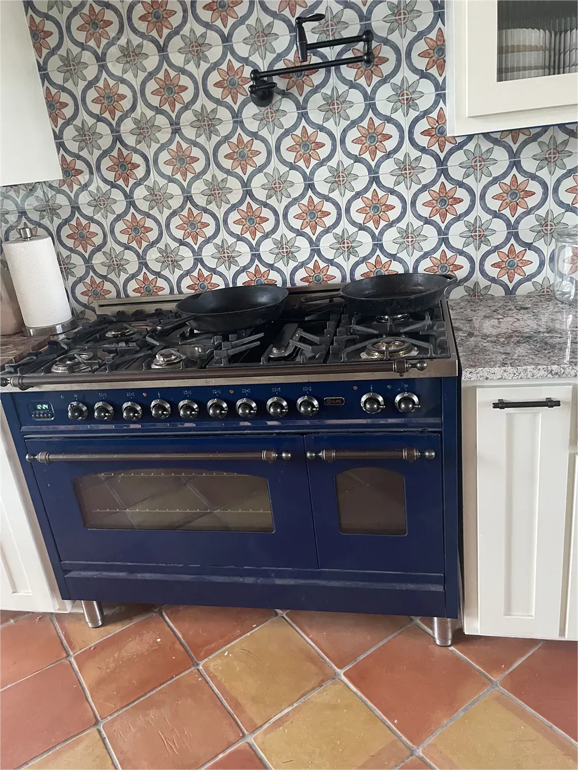 A blue stove top oven is sitting on a tiled floor in a kitchen.
