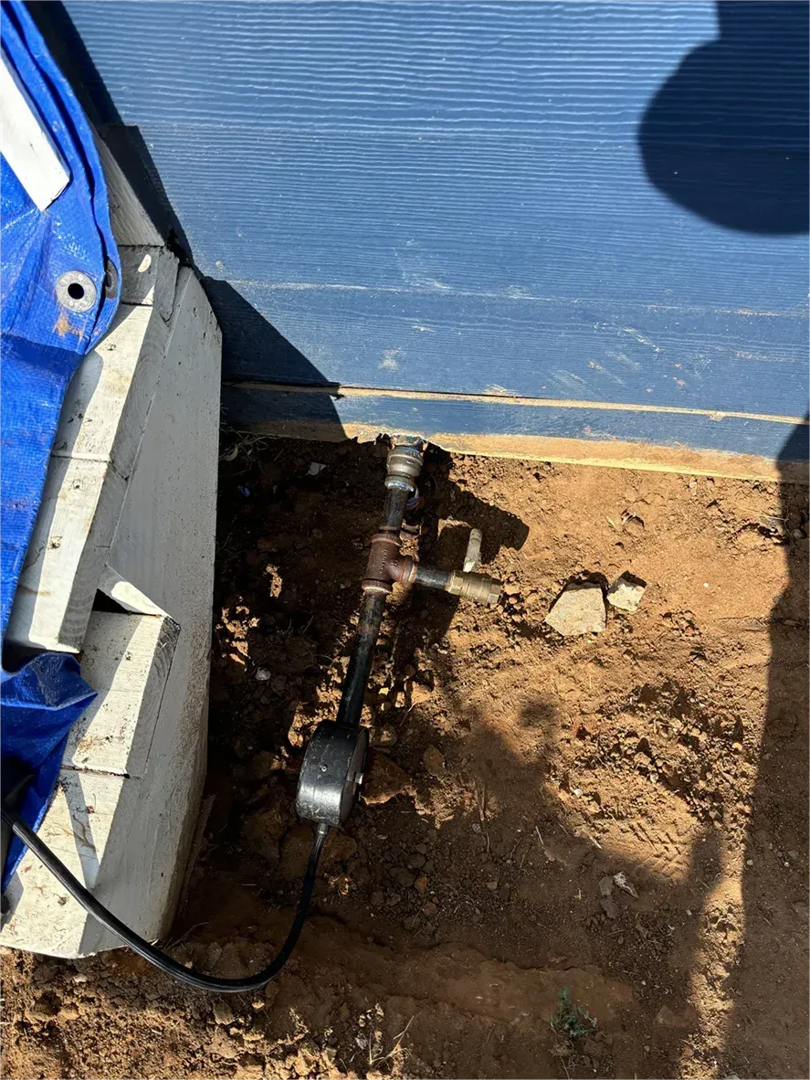 A hose is sitting in the dirt next to a blue tarp.