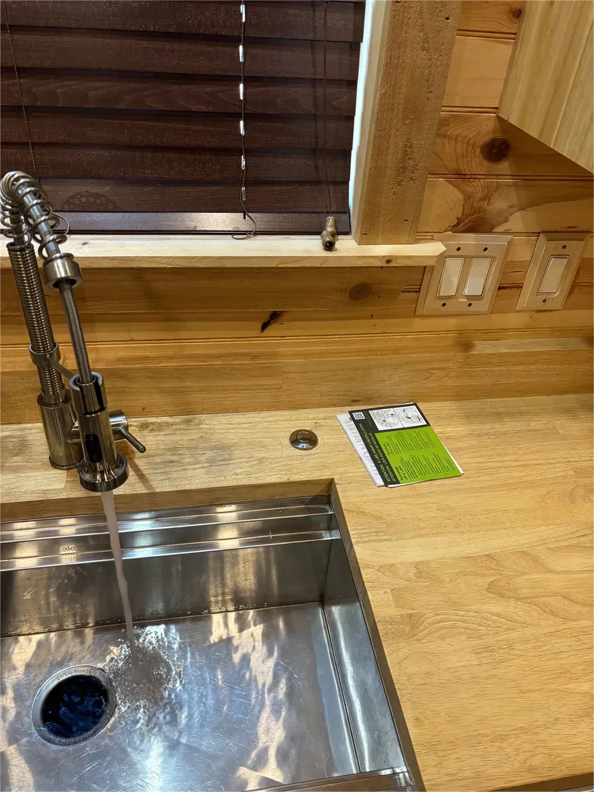 A kitchen sink with a faucet and a wooden counter top.