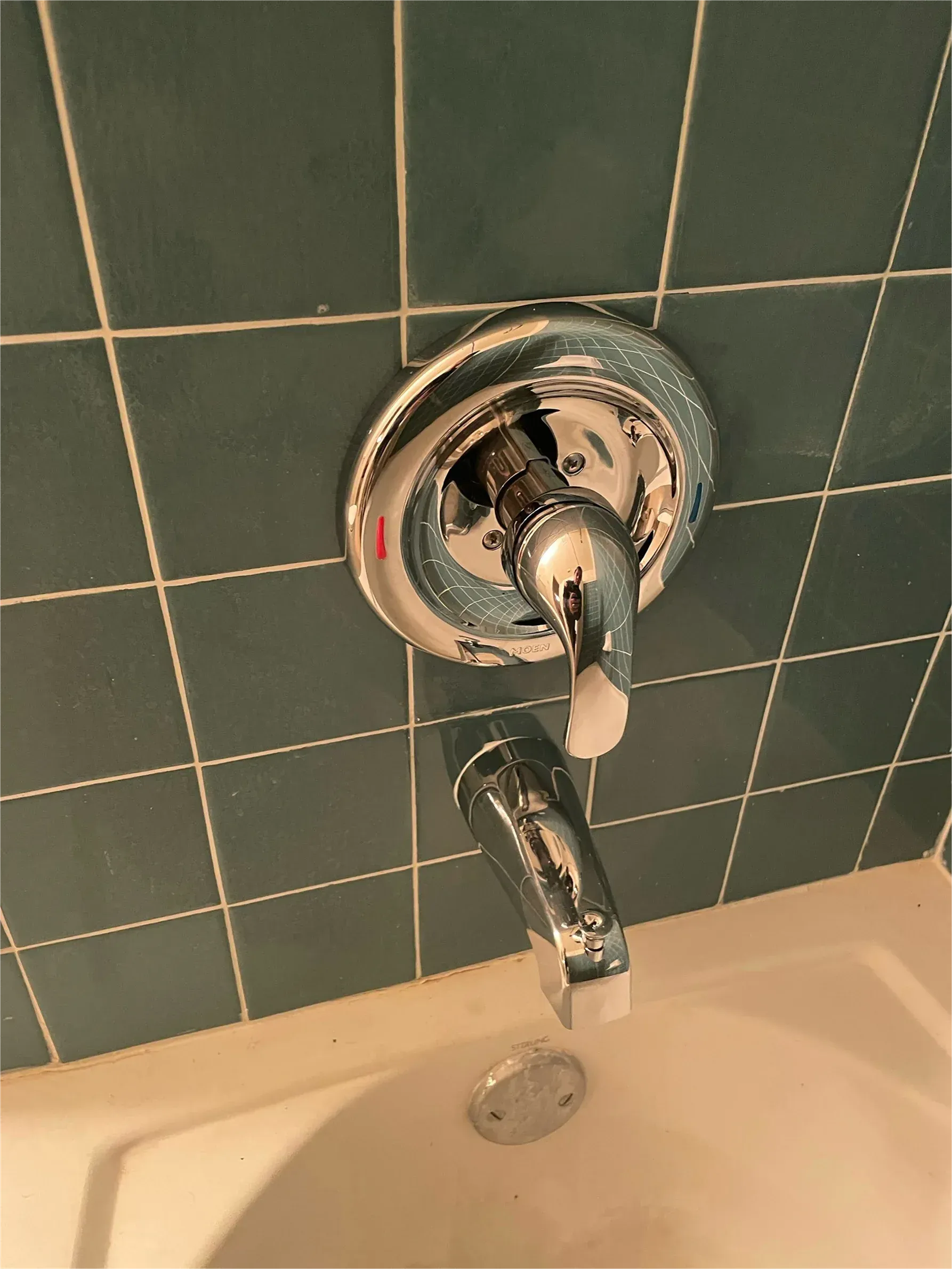 A close up of a shower faucet on a blue tiled wall next to a bathtub.