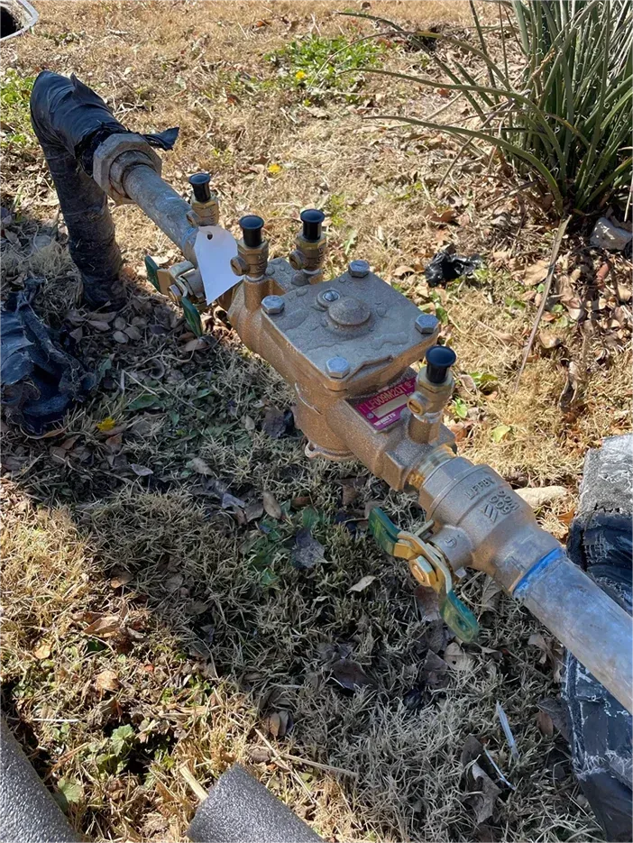 A water valve is sitting on the ground next to a pipe.