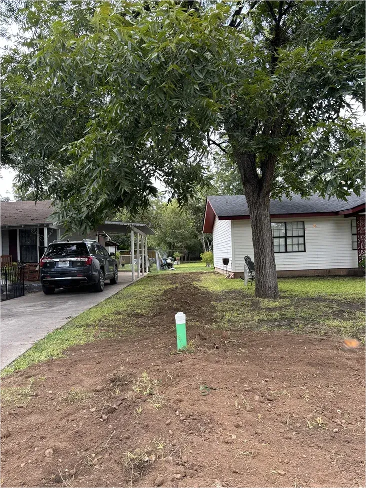 A car is parked in front of a house next to a tree.