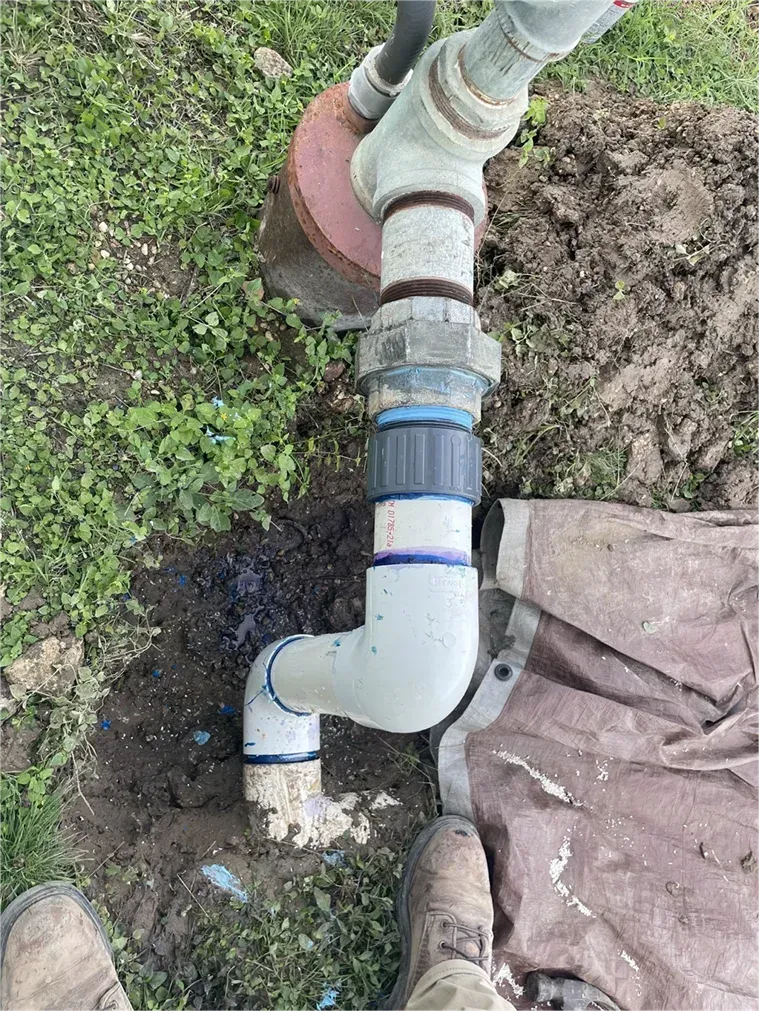 A person is standing next to a pipe in the dirt.