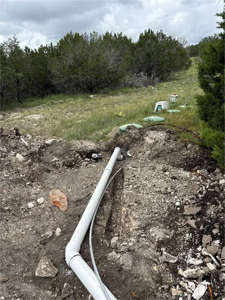 A white pipe is laying in the dirt in a field.
