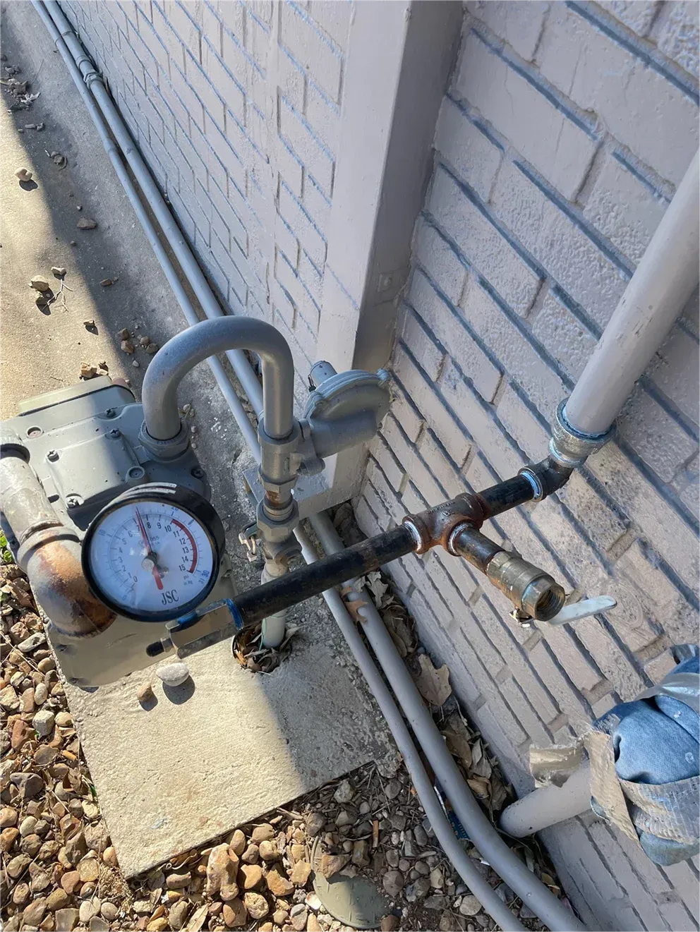 A pressure gauge is attached to a pipe on the side of a brick building.