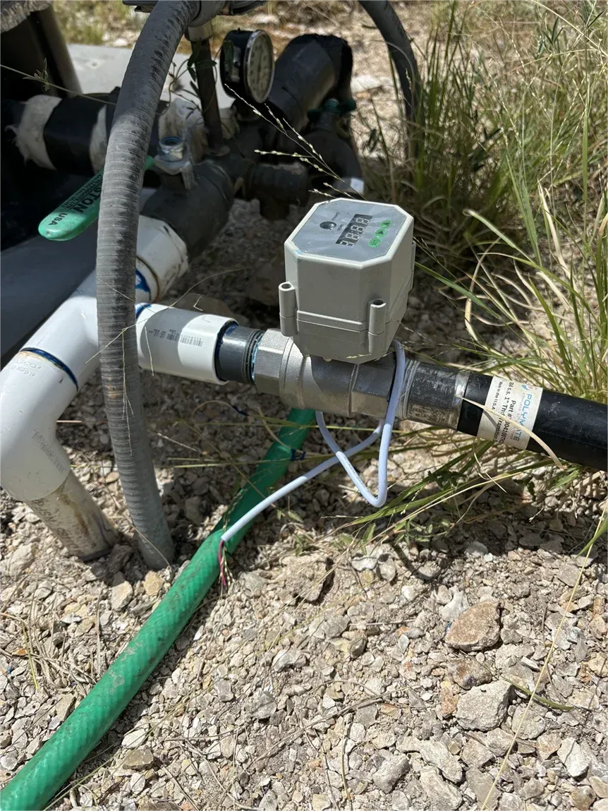 A water meter is attached to a pipe next to a green hose.