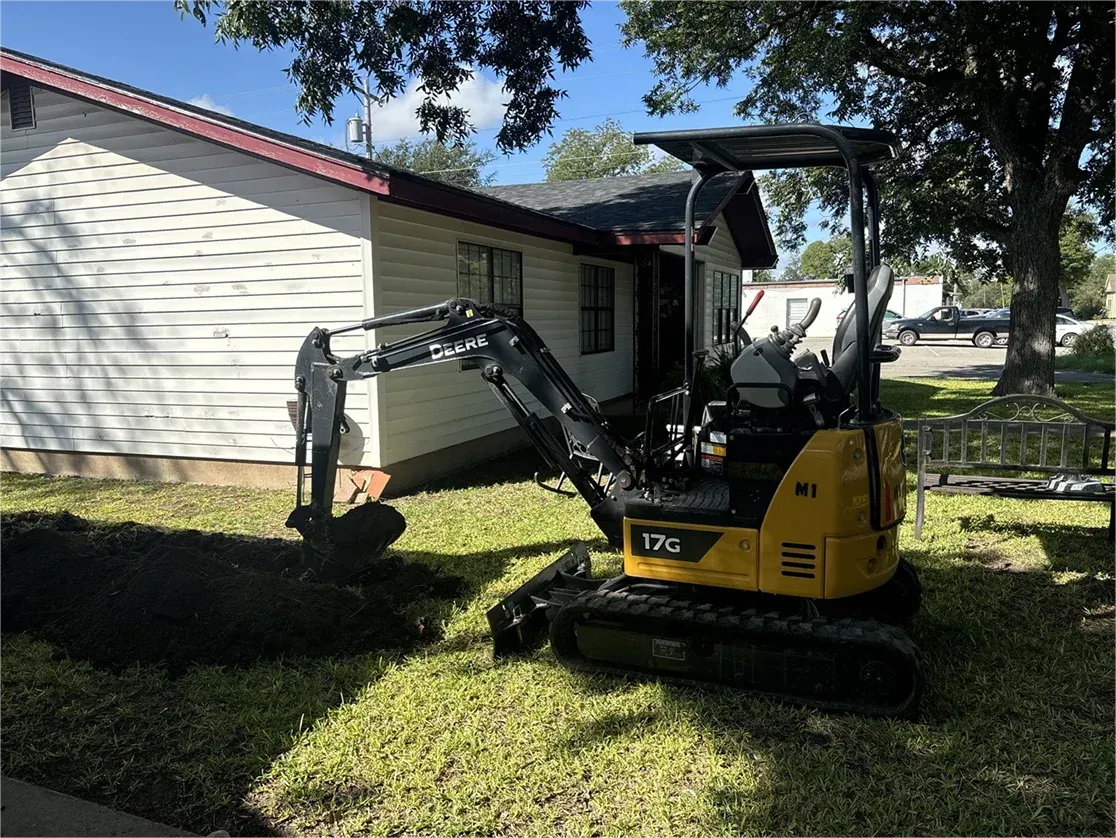 A small yellow excavator is parked in front of a house.
