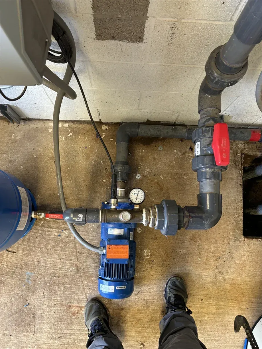 A person is standing next to a pump and pipes on the floor.
