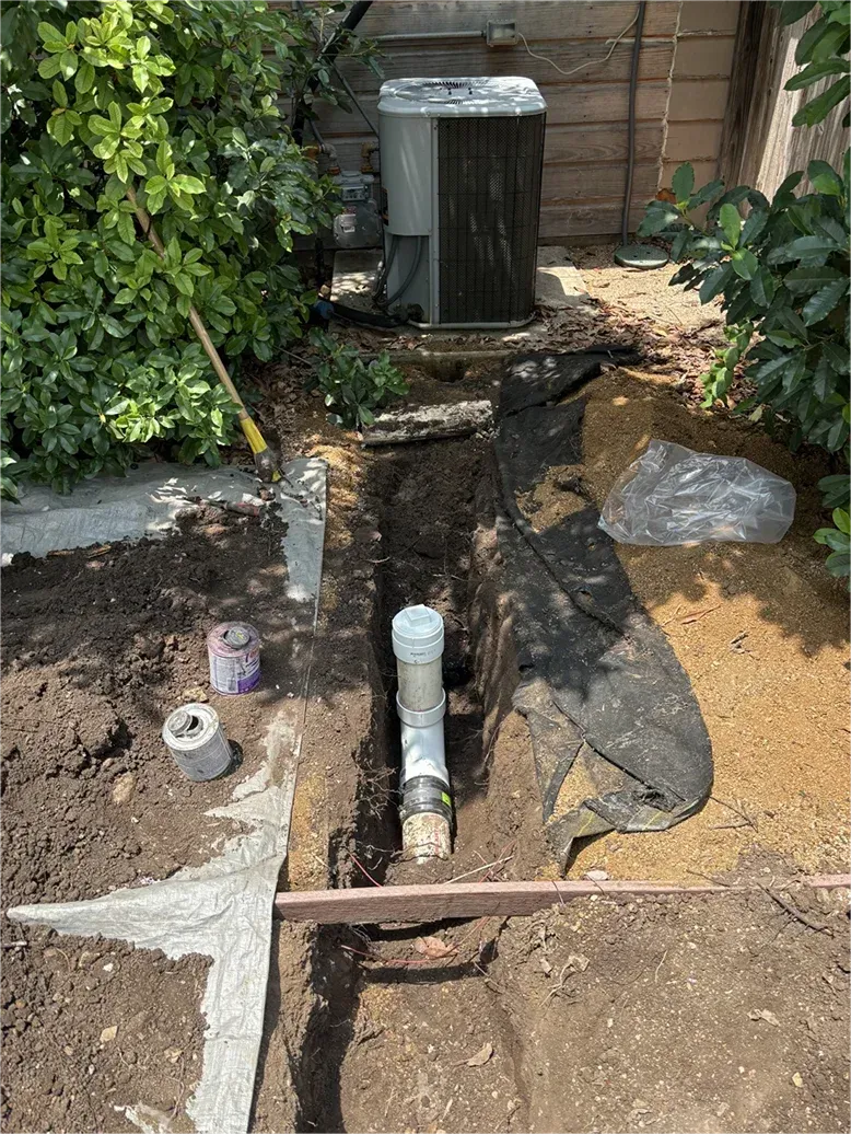 A drain pipe is being installed in the ground next to an air conditioner.