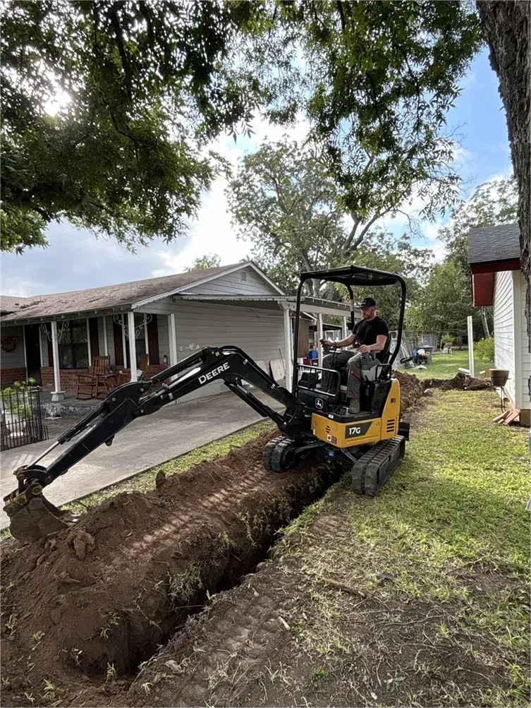 A man is driving a small excavator in front of a house.
