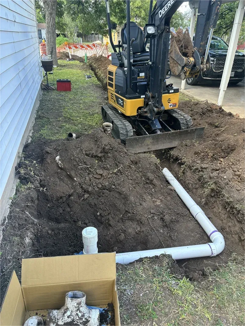 A small excavator is digging a hole in the ground in front of a house.