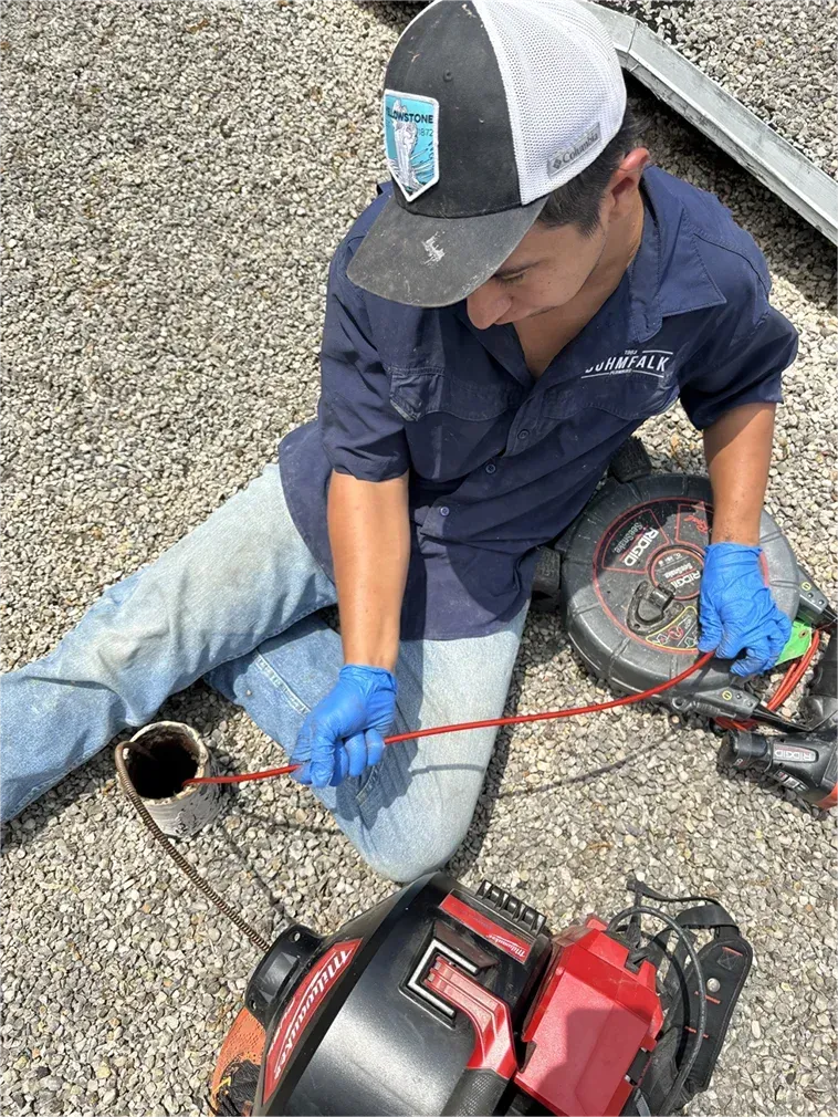 A man is kneeling down on the ground using a drain cleaner.