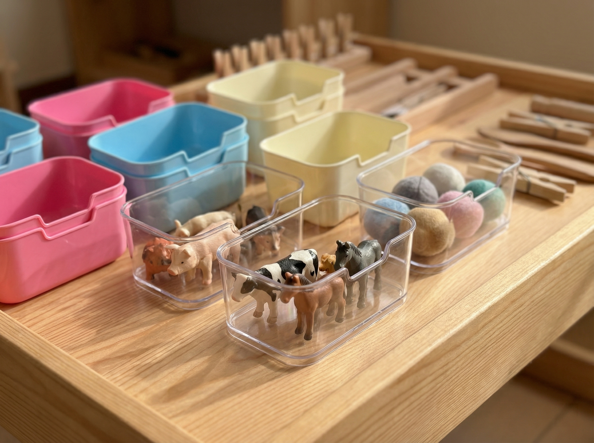 Sensorie Play sorting cups used for sensory organization, featuring pastel-colored containers filled with small felt balls and miniature farm animal figurines on a wooden table.