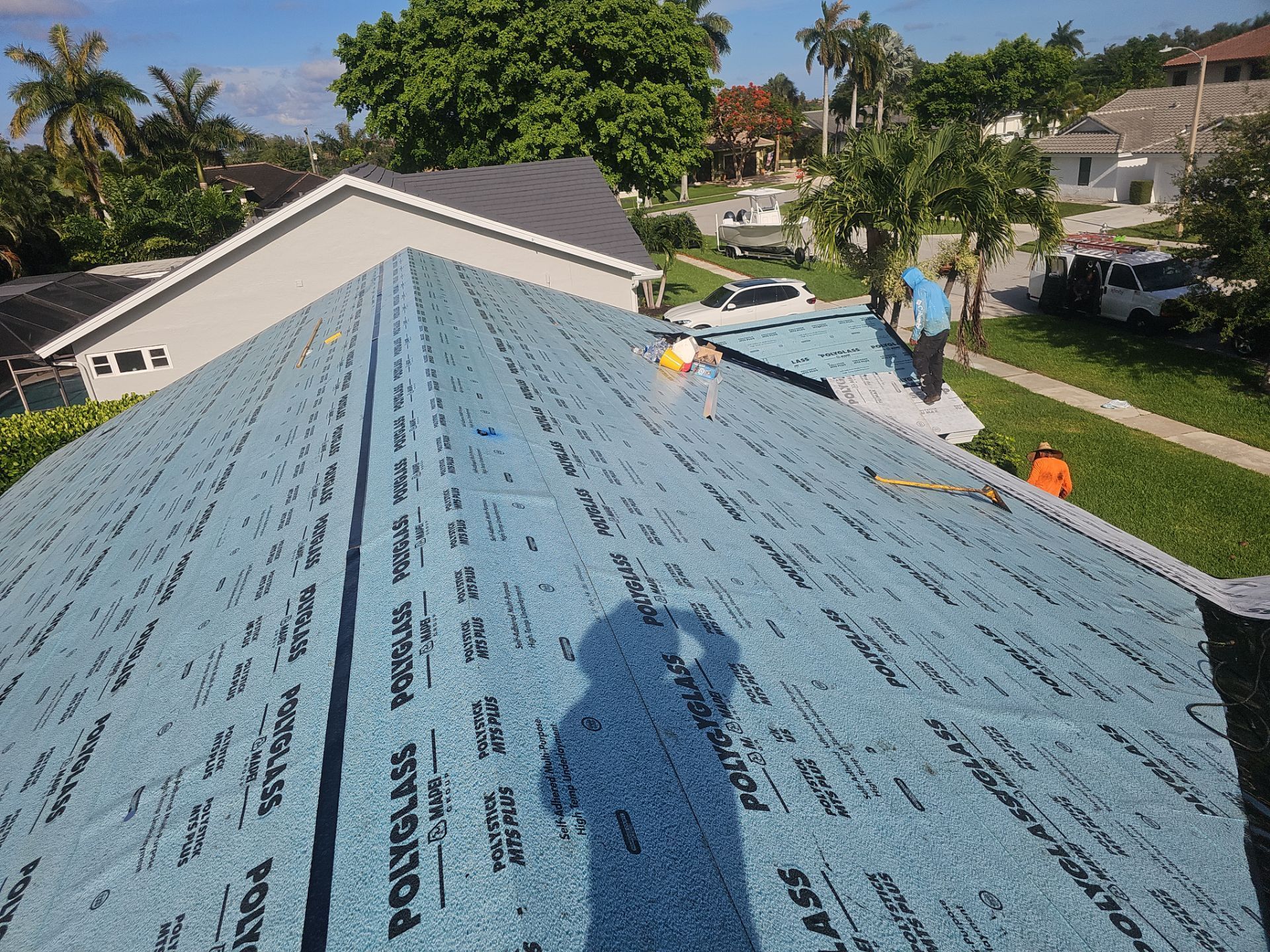 Roofers installing blue underlayment on a house roof in a sunny suburban neighborhood